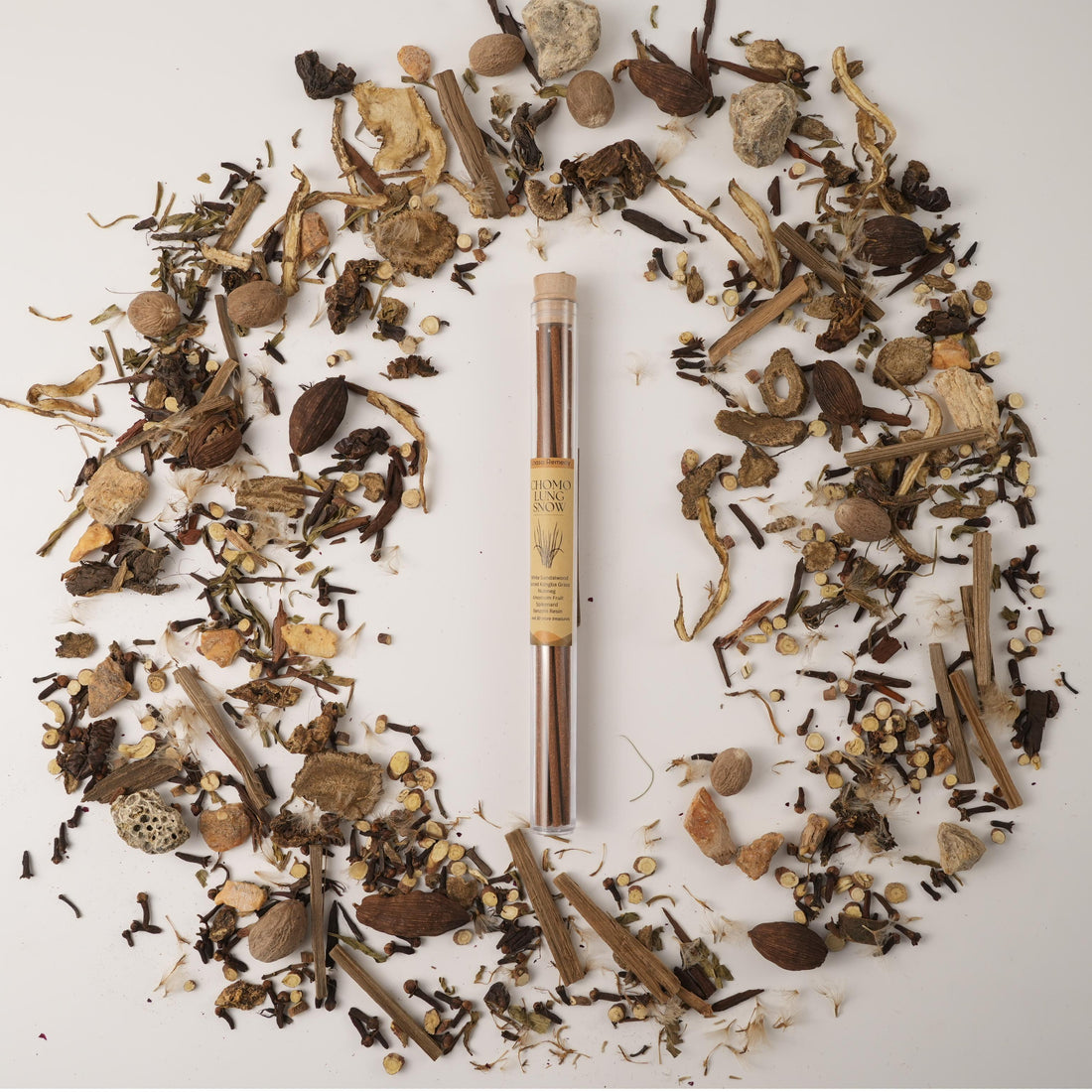 Chomolung Snow Tibetan incense sticks in a glass tube, surrounded by traditional Chinese medicinal herbs on a white background.