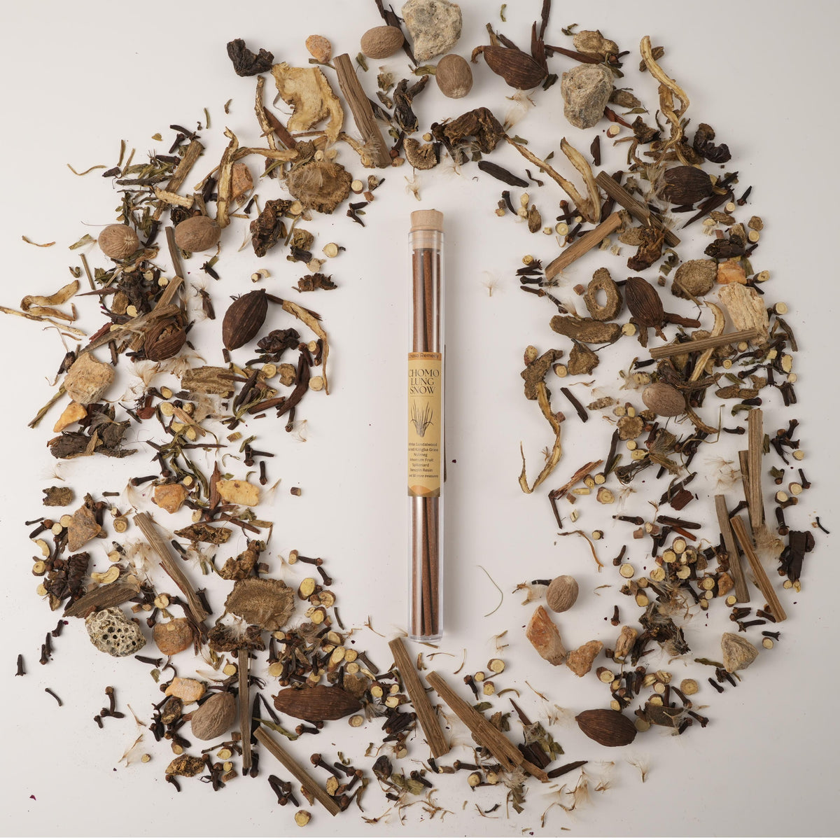 Chomolung Snow Tibetan incense sticks in a glass tube, surrounded by traditional Chinese medicinal herbs on a white background.