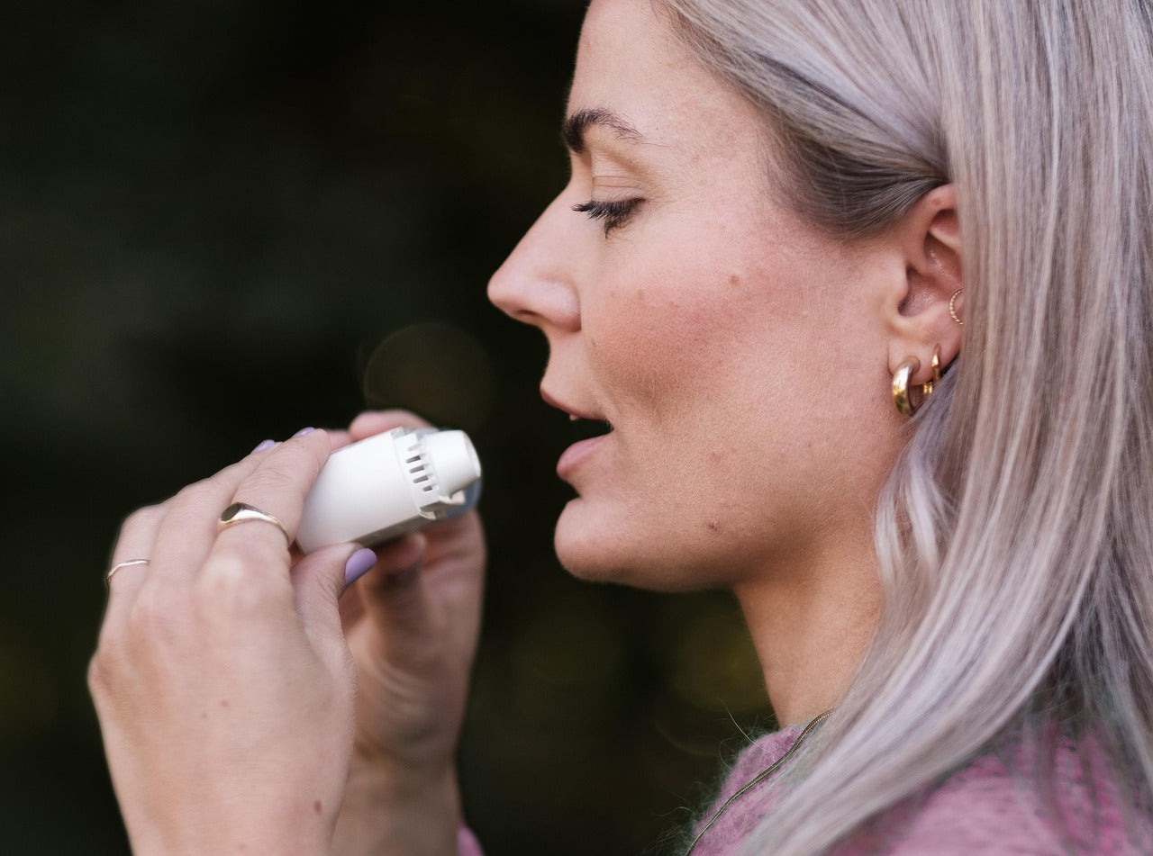 Side profile of a woman using a small white inhaler for breathing support.