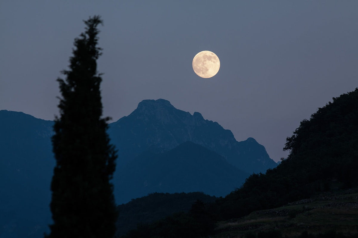 A glowing full moon rising over blue mountain silhouettes at dusk, symbolizing the spiritual energy peak and ideal time for ritual release during full moon cleansing.