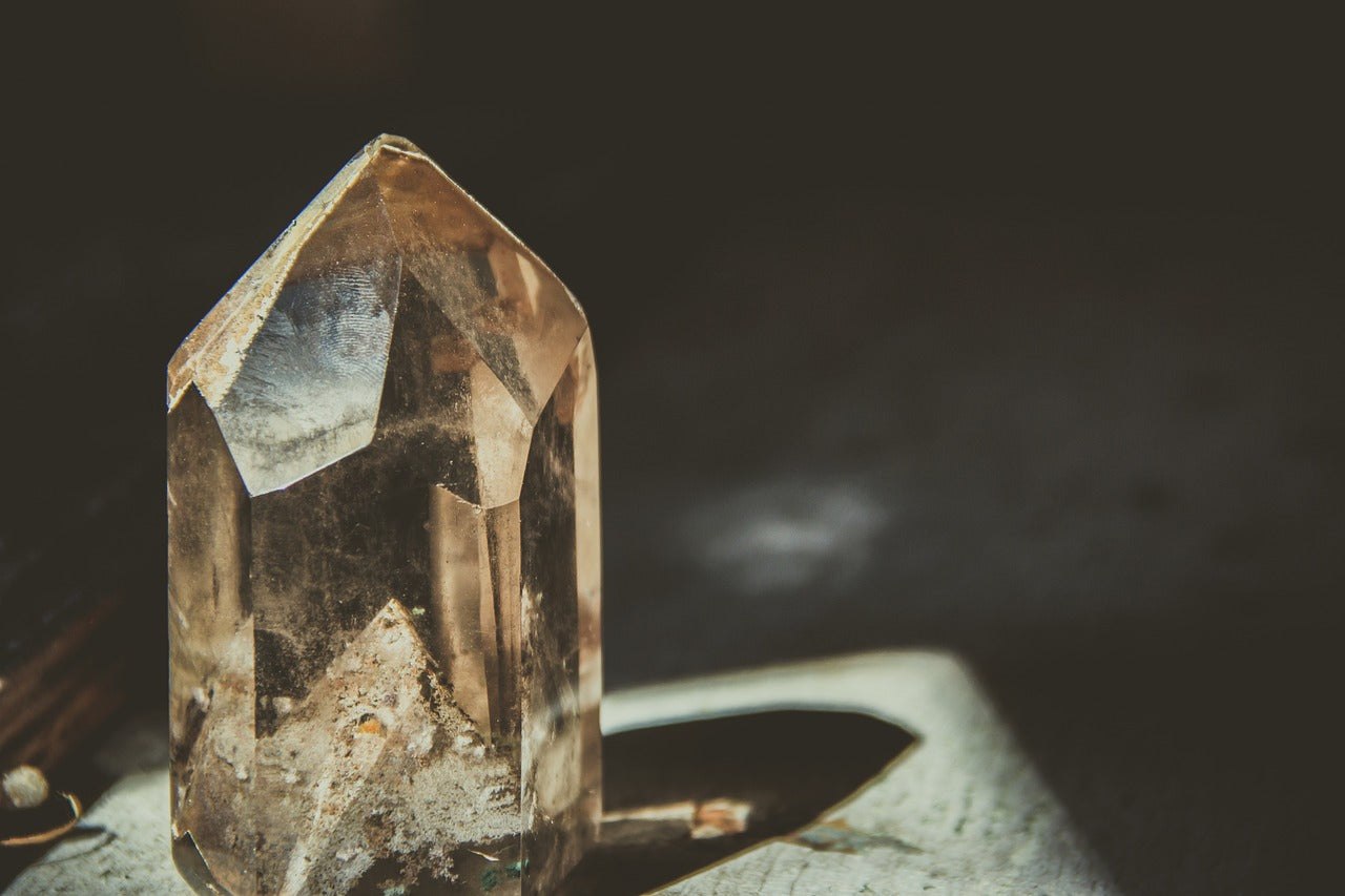 A clear quartz crystal resting on a wooden table, reflecting light and showcasing its natural facets.