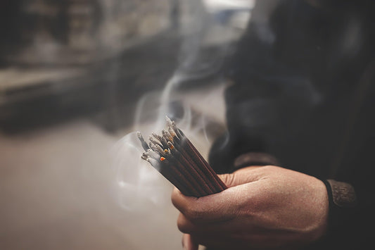 Hand holding burning Tibetan incense sticks with gentle smoke rising during a ritual