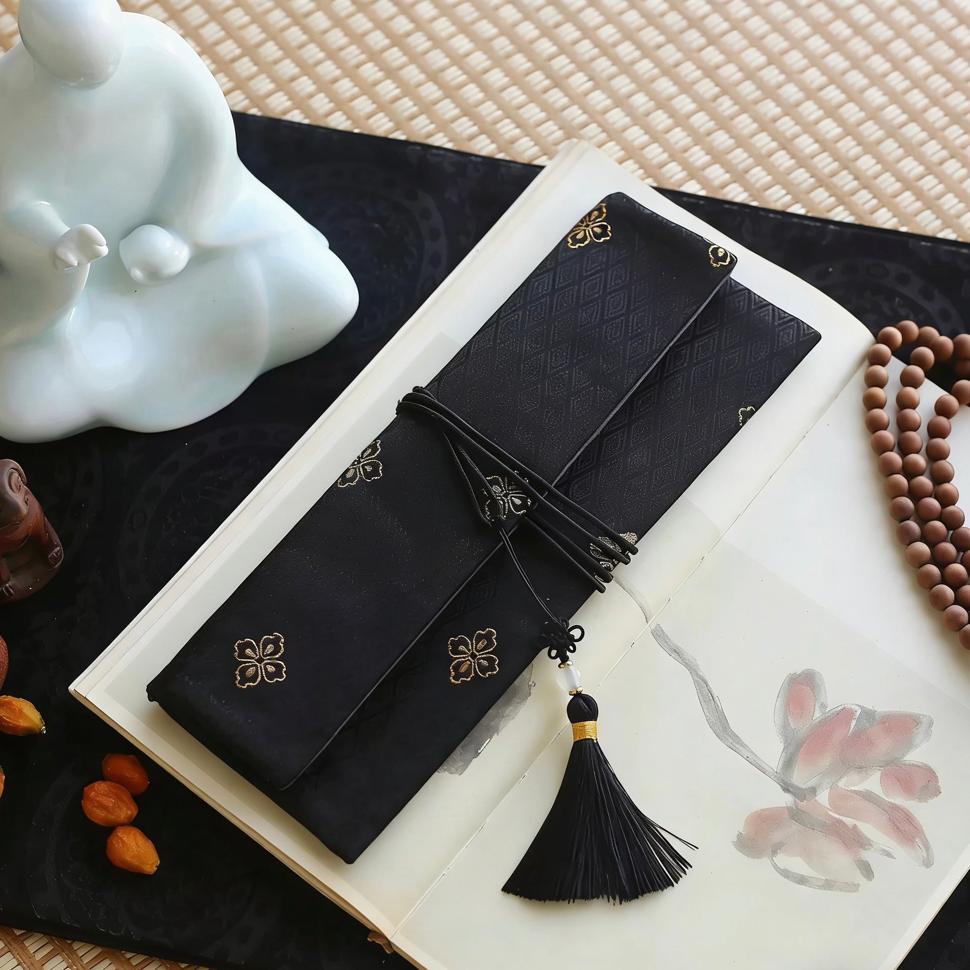 Black silk incense carry pouch with subtle gold woven pattern and a black tassel with gold accent, placed on an open art book atop a dark cloth