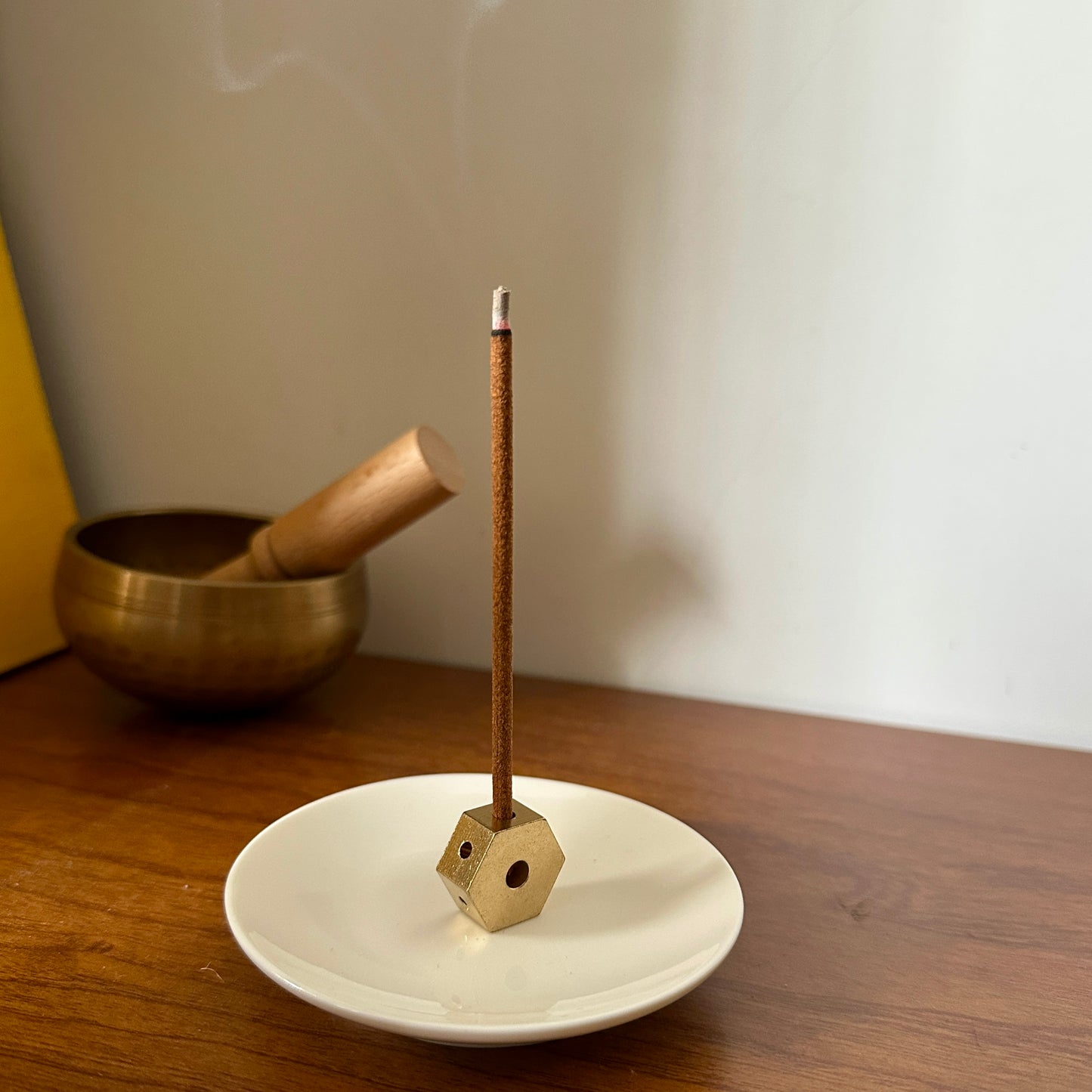 Brass 4-hole incense holder placed on a white ceramic plate with a Tibetan incense stick burning on a wooden surface