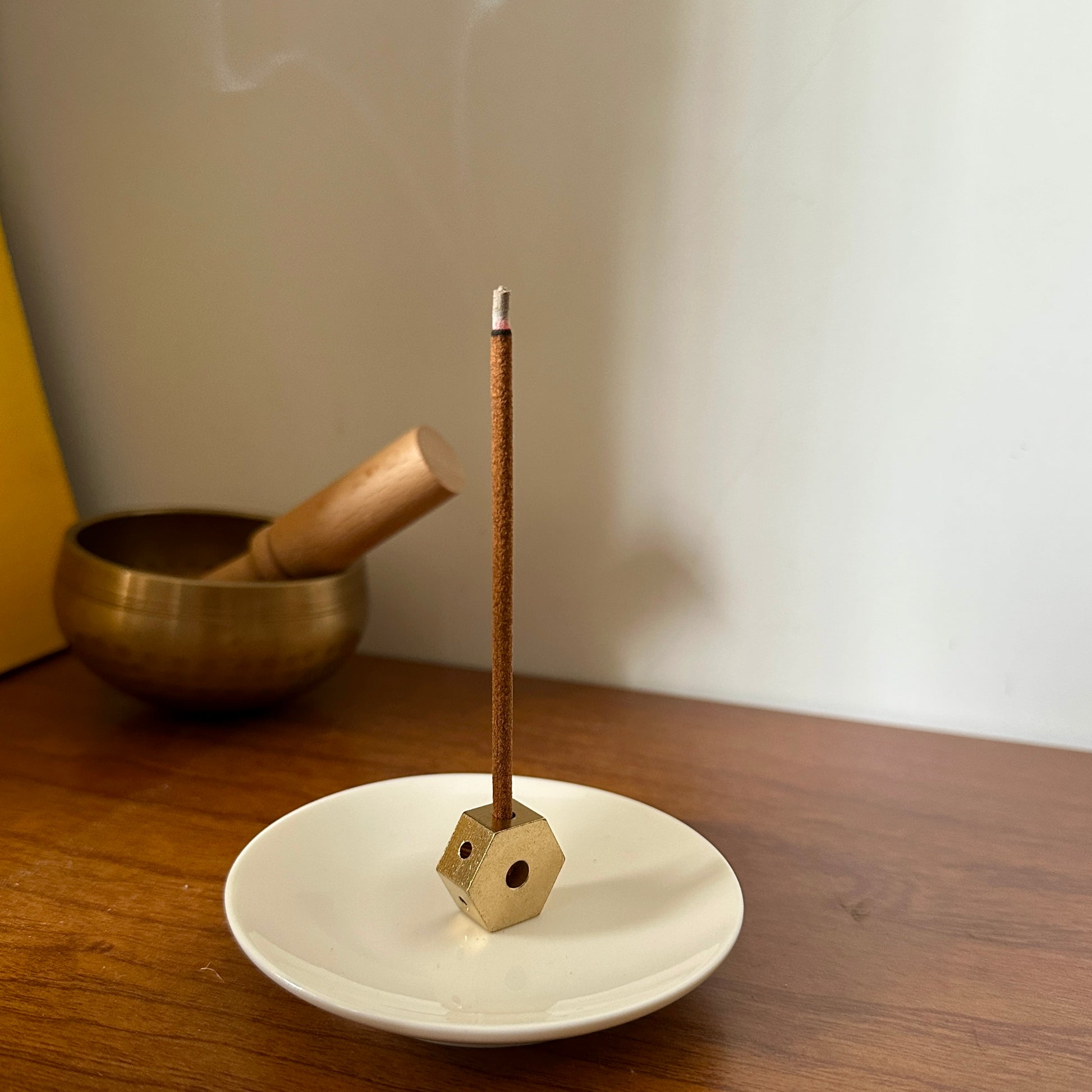 Brass 4-hole incense holder placed on a white ceramic plate with a Tibetan incense stick burning on a wooden surface