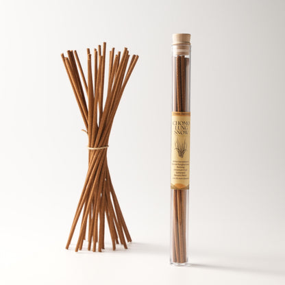 A bundle of Chomolung Snow Tibetan incense sticks tied with a string, placed beside a labeled glass tube containing the same incense, set against a minimalist white background.