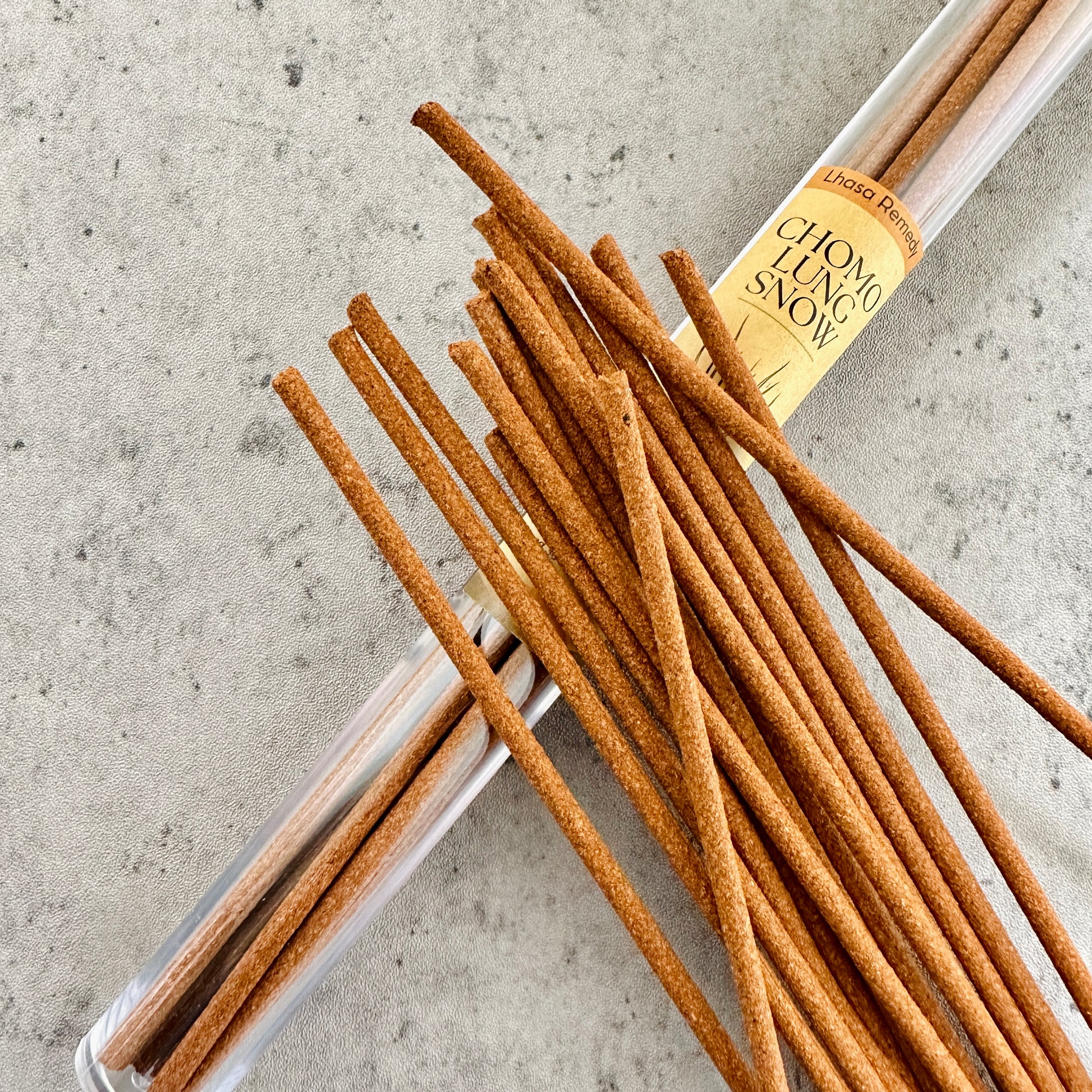 Chomolung Snow Tibetan incense sticks spilling from a clear tube onto a light stone background, evoking a sense of purity, coolness, and spiritual cleansing.