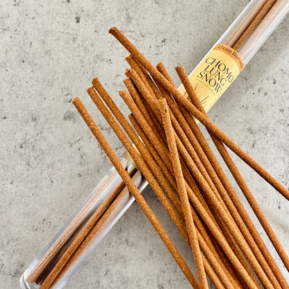Chomolung Snow Tibetan incense sticks spilling from a clear tube onto a light stone background, evoking a sense of purity, coolness, and spiritual cleansing.