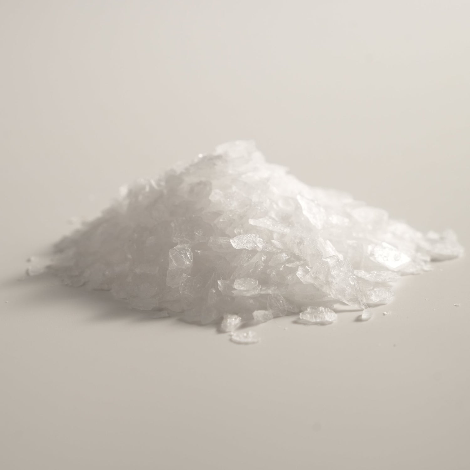 A close-up of natural borneol crystals used in Traditional Chinese Medicine, shown as a small white pile with translucent, flake-like texture on a soft neutral background.
