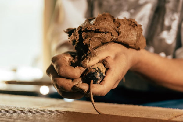 Hands pressing herbal incense dough through a traditional tool to form incense sticks.