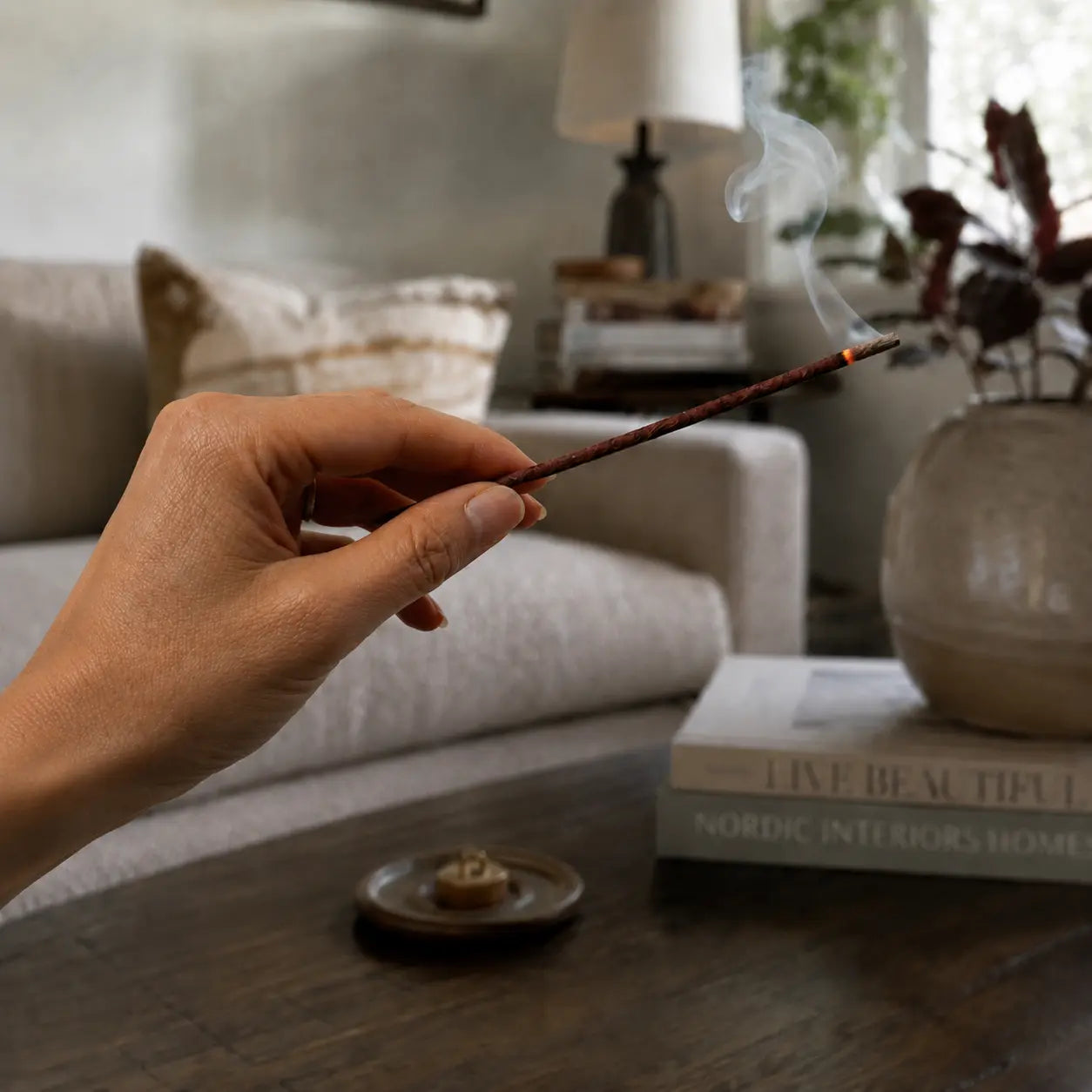 Hand holding burning Lhasa Remedy Buddhas Mandala Tibetan herbal incense stick in living room lifestyle