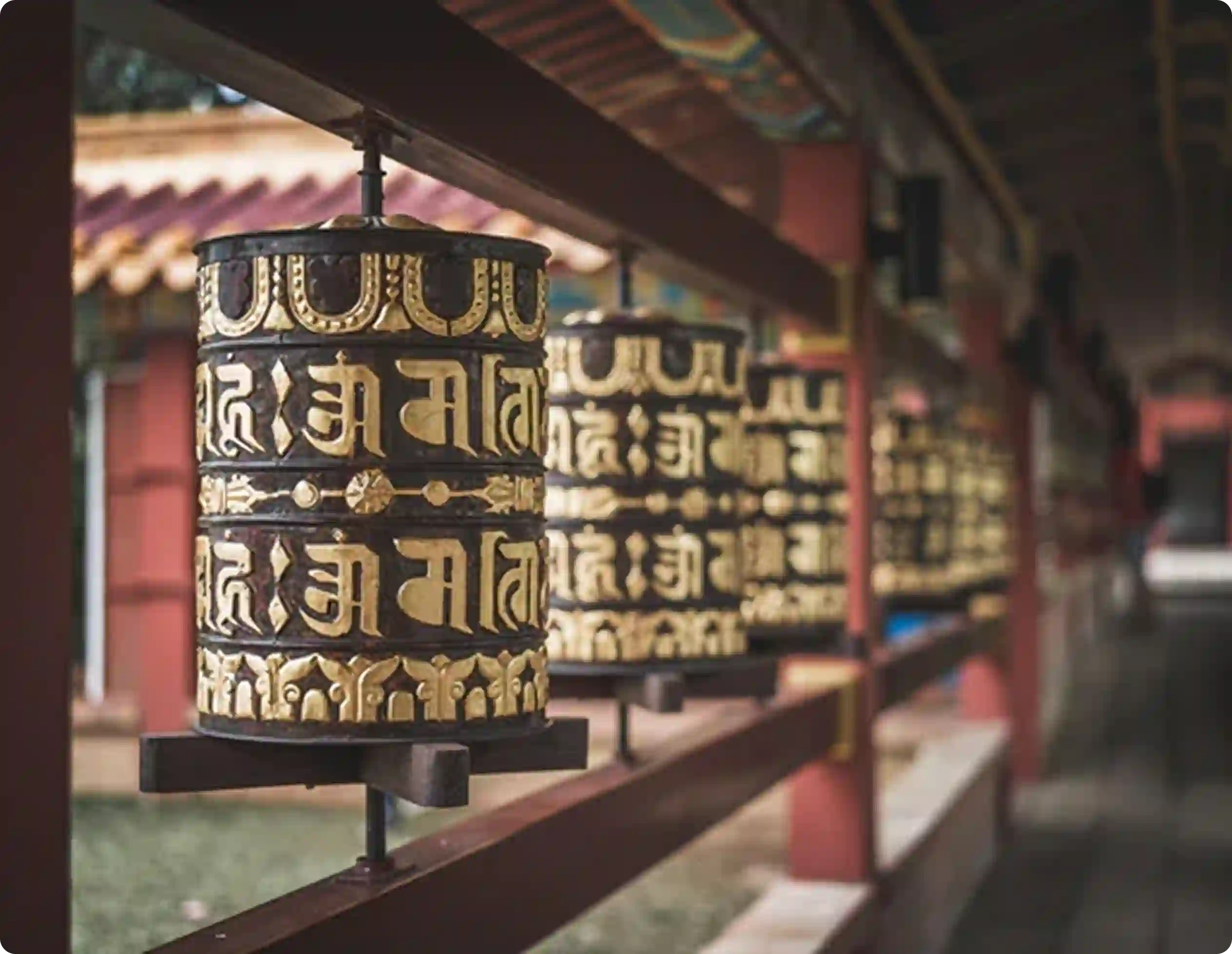 Row of Tibetan Buddhist prayer wheels with gold Om Mani Padme Hum mantra script at monastery temple