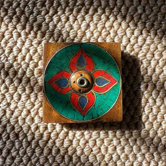 Lotus Blossom Incense Holder with hand-painted red, green, and blue floral design, centered on a square wooden base and placed on a woven mat in natural light.
