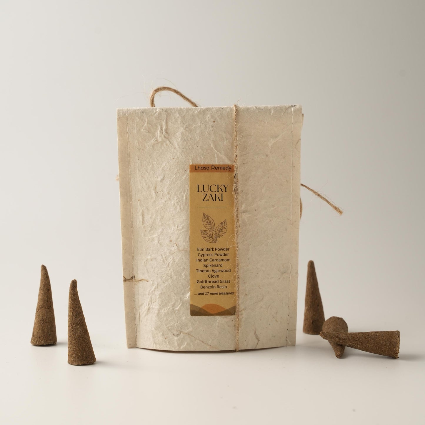 Lucky Zaki incense cones arranged beside a handmade textured paper package bag with a product label, placed on a minimal off-white background.