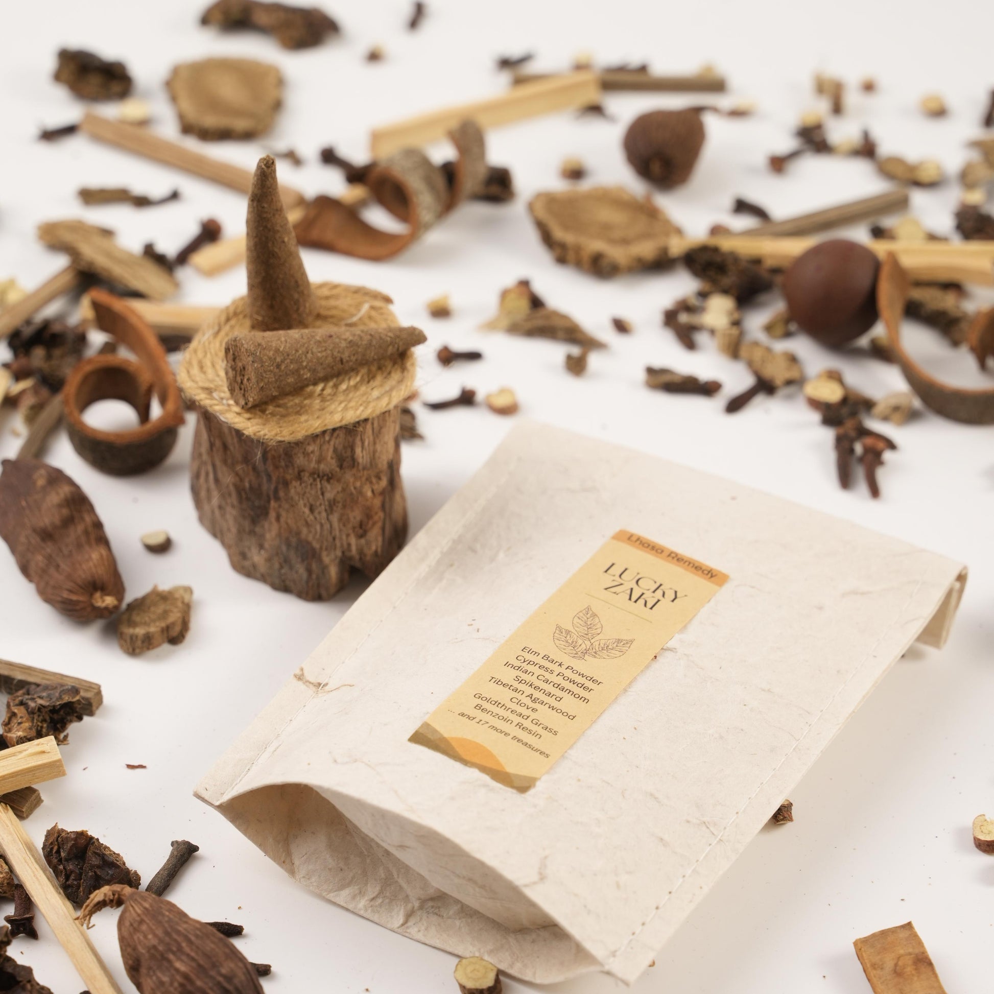 Lucky Zaki Tibetan incense cones and packaging surrounded by aromatic herbs and spices used in Traditional Chinese Medicine, including cardamom, cloves, and cinnamon, styled on a white background.