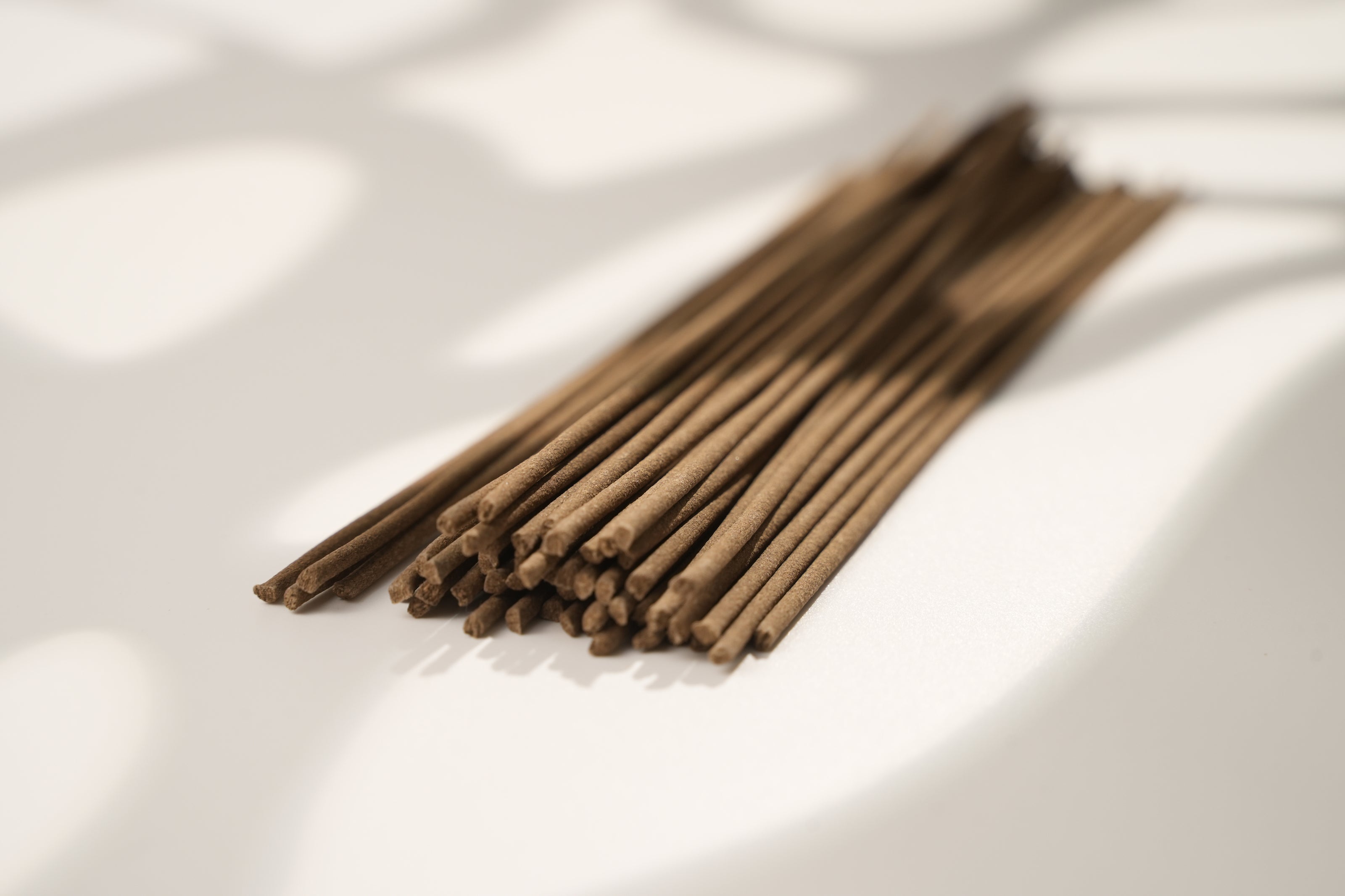 A bundle of brown, hand-rolled Tibetan incense sticks lying on a white surface with soft, natural shadows.