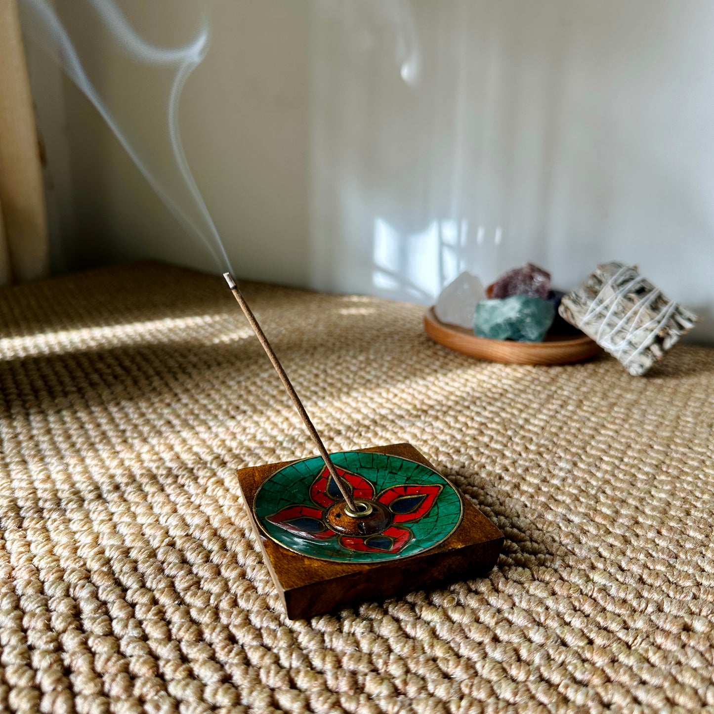 Nimu Village Tibetan incense stick burning on Lhasa Remedy’s Lotus Blossom holder, with gentle smoke curling up beside crystals and sage in a serene, sunlit space.