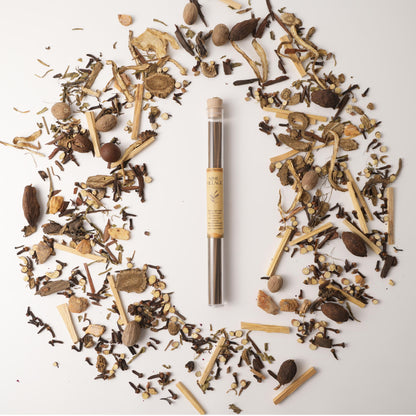 Nimu Village Tibetan incense sticks in a glass tube, laid on a bed of traditional Chinese medicinal herbs over a white background.