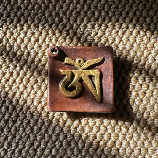 Sacred OM Ceramic Incense Holder with a raised golden Tibetan Om symbol on a handcrafted ceramic base, resting on a textured woven mat.