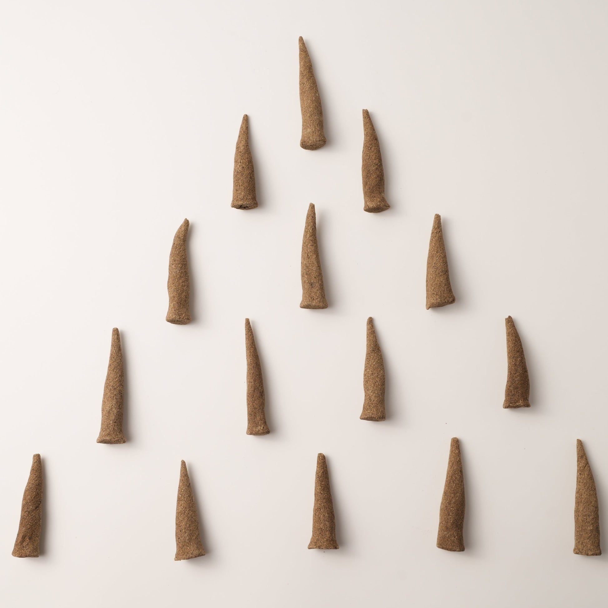 A minimalist top-down image of Sera Serene Tibetan incense cones arranged in a symmetrical triangle on a light background. These handcrafted cones are made with calming herbs used in Tibetan medicine to support clarity, focus, and inner peace.