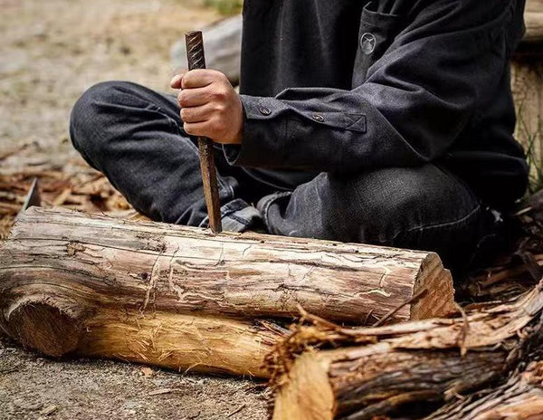 Artisan sitting on the ground and splitting aromatic wood logs with a hand tool for incense making.