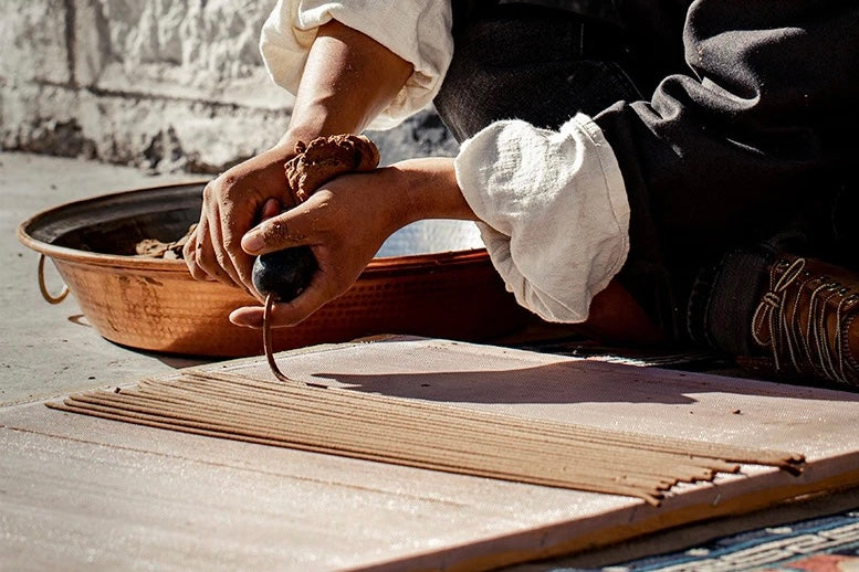 Close-up of a Tibetan artisan hand-rolling incense sticks using traditional tools and natural ingredients under the sun.