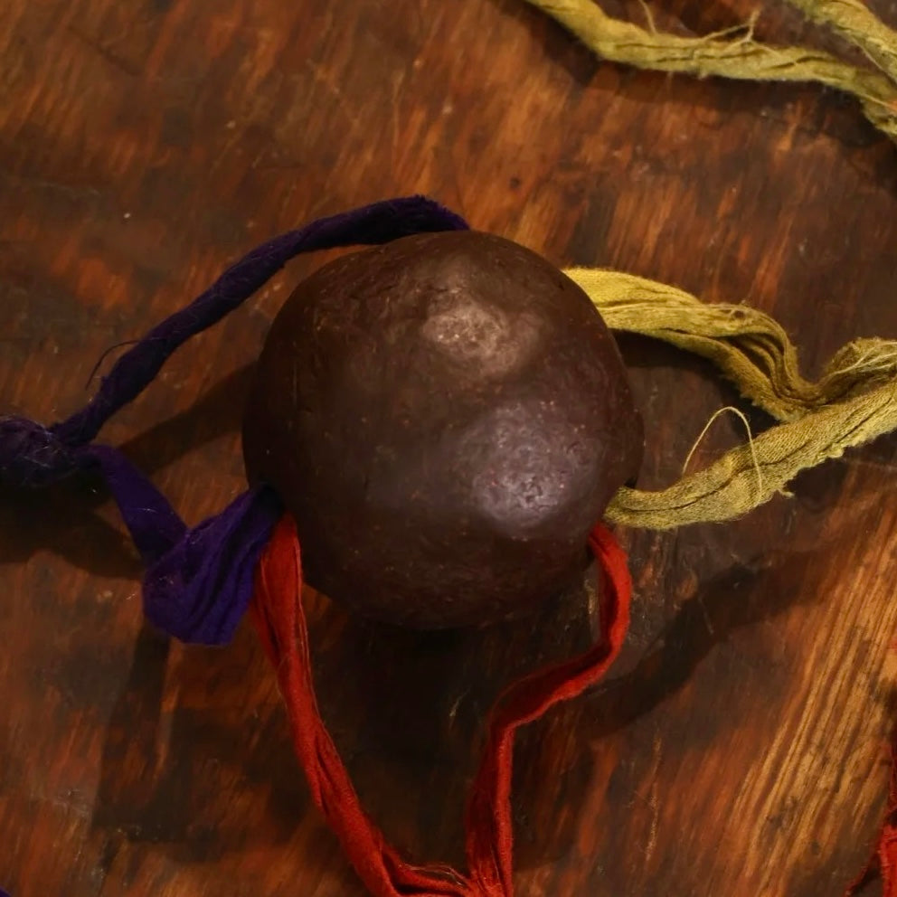 A sacred nectar pill from Zaki Temple, wrapped with multicolored threads and placed on a wooden surface. Traditionally made with rare herbs and blessed substances, this pill is used in Tibetan rituals for healing, protection, and spiritual empowerment.